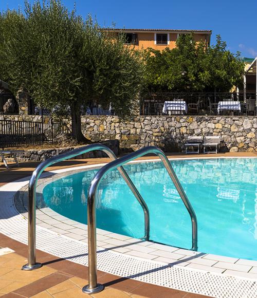 Piscina con lettini e ombrelloni blu, vista attraverso foglie.