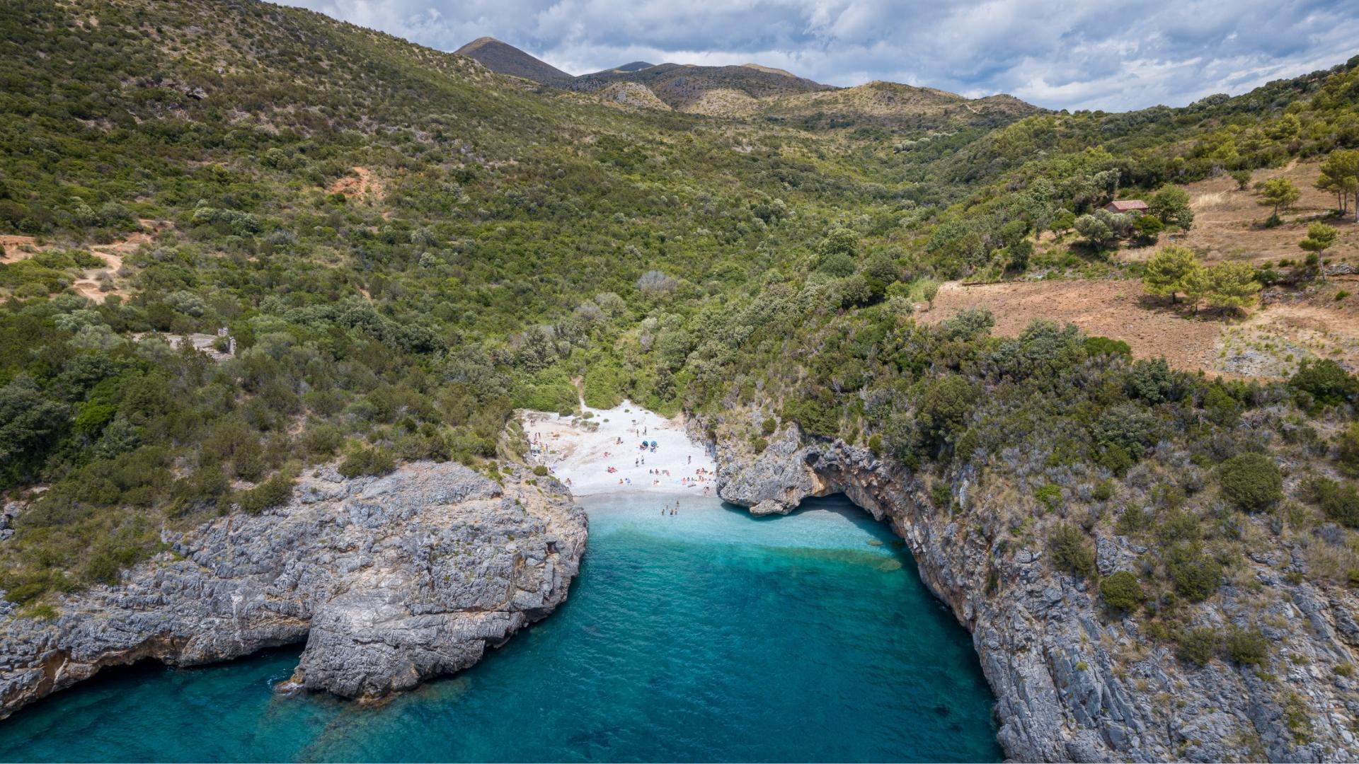 Spiaggia nascosta tra le rocce con acque turchesi e vegetazione lussureggiante circostante.