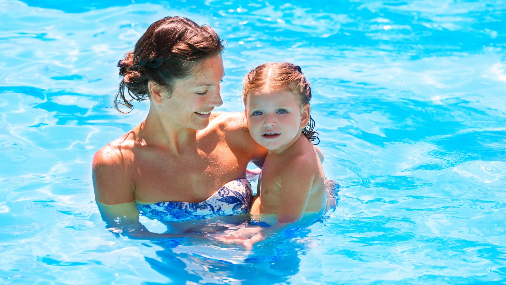 Madre e figlio sorridono insieme in piscina, immersi nell'acqua azzurra.