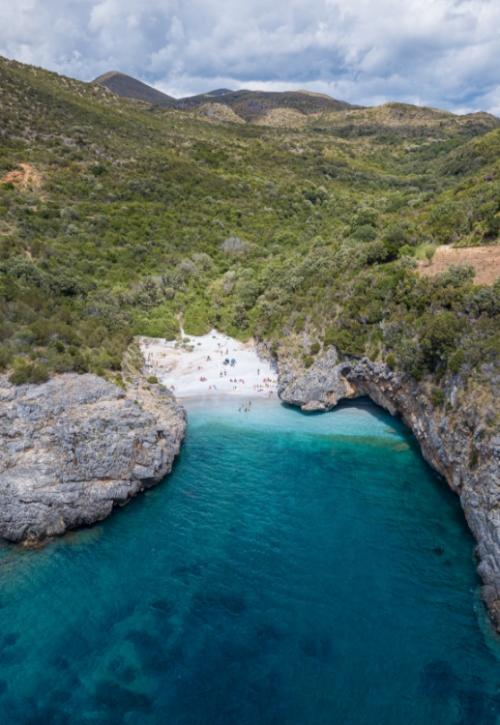 Spiaggia nascosta tra rocce e vegetazione, con acqua cristallina e sabbia bianca.