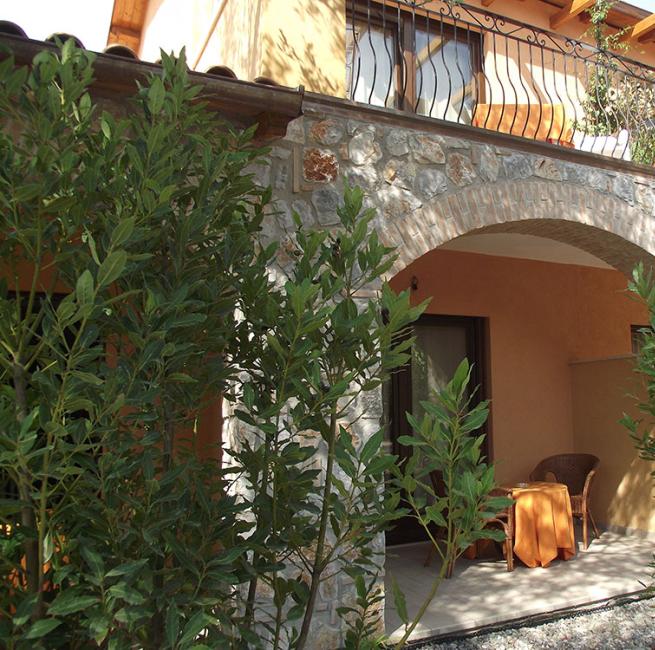 Portico in pietra con tavolino e sedia, circondato da piante verdi.