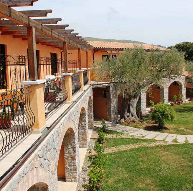 Edificio rustico con balconi in ferro battuto e giardino con ulivi.