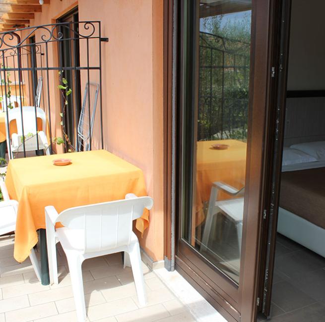 Terrazza con tavolo, sedie bianche e camera da letto con letto matrimoniale.