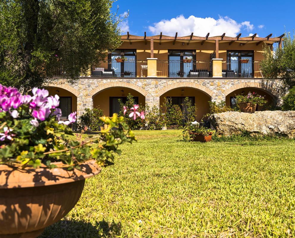 Edificio a due piani con archi in pietra, giardino e cielo nuvoloso.